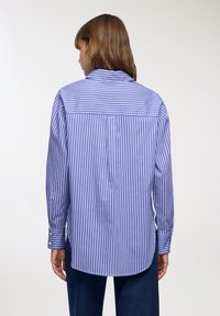 Camicia a maniche lunghe a righe blu e bianche con yoke posteriore, polsini con bottoni e orlo leggermente curvato. Realizzata in tessuto leggero.