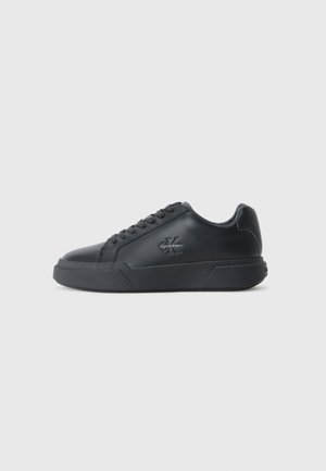 Czarny, niski skórzany sneaker z sznurowaniem z przodu i logo Calvin Klein po boku, ustawiony na jednolitym jasnoszarym tle.