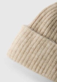 Beige ribitud kudumisega müts pehmest villast, millel on volditud äär ja tekstureeritud viimistlus. Ideaalne soojuseks ja mugavuseks.