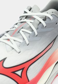 Scarpa da ginnastica bianca con tomaia testurizzata, dettagli rossi e chiusura con lacci. Elementi di design notevoli includono un logo a contrasto e una suola intermedia vibrante.