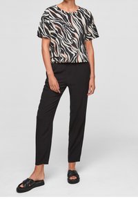Top de manga corta con un patrón de olas en blanco y negro, combinado con pantalones negros ajustados y sandalias planas negras. Textura de tela suave.