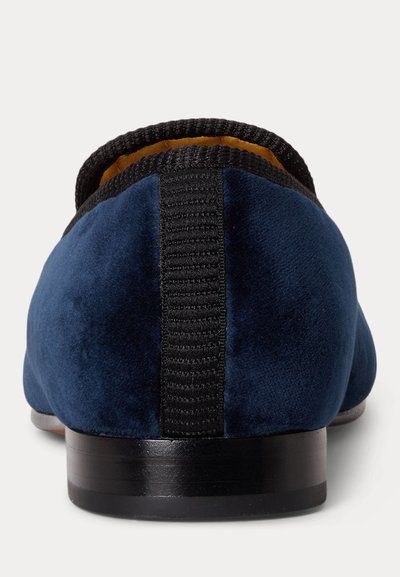 Pogled od zada na mornarsko modri žametni loafers z črnimi rebrastimi robovi in črnim nizkim petom na belem ozadju.