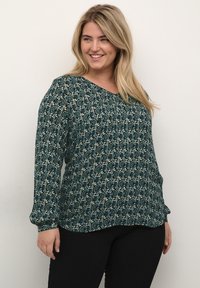 Langærmet bluse i mørk teal med et blomstermønster i lys blå og creme. Har V-hals og løs pasform, lavet af let stof.