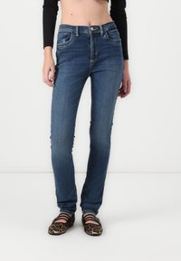 Fitted dark blue jeans with five pockets, belt loops, and slight whiskering, paired with leopard print flats featuring cross straps.