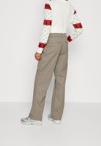 Szare, teksturowane spodnie typu szerokie nogawki z wysokim stanem i tylnymi kieszeniami, zestawione z białym sweterkiem z czerwonymi i czarnymi wzorami świątecznymi.