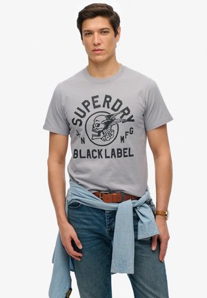 Grå bomulds t-shirt med et sort grafisk print af et kranium og terninger. Sæt sammen med blå jeans og en lyseblå skjorte knyttet om livet.