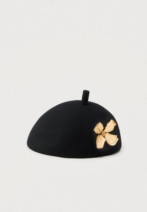 Beret negru din fetru cu o formă rotunjită, având un accent floral texturat auriu pe o parte și o mică buclă în partea de sus.