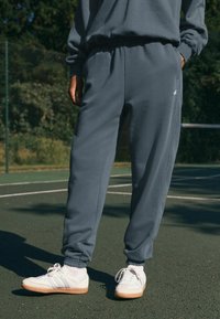 Grijze sweatpants van zachte stof met een elastische tailleband en boorden; gecombineerd met witte sneakers met tan kleurige zolen en veters.