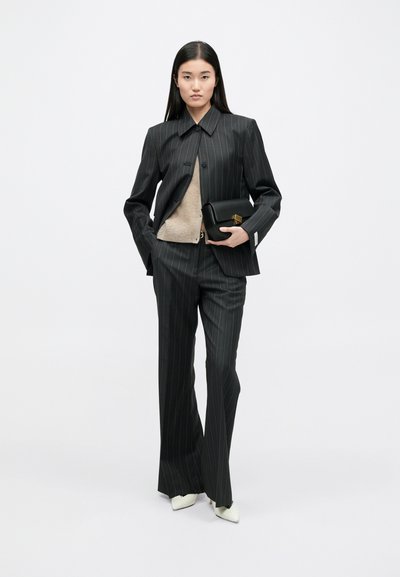 Mustaline triipudega ülikond, millel on kohandatud jope ja laiad püksid, koos beezist kootud toppi ja väikese musta käekotiga. Valged terava ninaga kingad.