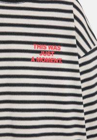 Zwart-wit gestreepte stof met rode tekst in het midden: "DIT WAS SLECHTS EEN MOMENT."