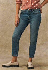 Middenhoge, recht gesneden denim jeans in donkerblauw, gecombineerd met off-white instappers; een casual, gepolijst uiterlijk met een zachte textuur.