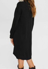 Abito nero a maglia con vestibilità rilassata, texture a coste sulle spalle, maniche lunghe e lunghezza fino al polpaccio. Abbinato a stivali neri al ginocchio.