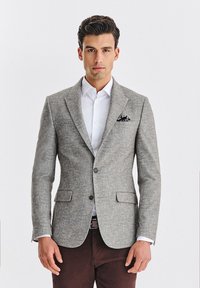 Jasnoszary żakiet wykonany z teksturowanej tkaniny, z klapami, dwoma przednimi kieszeniami oraz czarno-białą chusteczką w kieszeni.