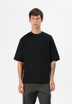 Sort bomulds T-shirt med rund halsudskæring og korte ærmer, der har en afslappet pasform og glat tekstur. Båret med grå cargobukser.