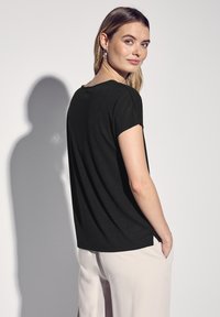 T-shirt nera a maniche corte con scollo rotondo, caratterizzata da un fit rilassato e spacchi laterali, abbinata a pantaloni larghi beige chiaro.
