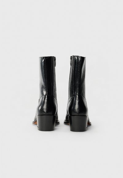 Botas de tobillo de cuero negro con un acabado texturizado, cierre lateral con cremallera y tacón cuadrado. El diseño presenta una silueta elegante y ajustada.