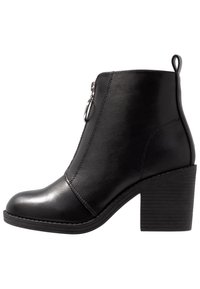 Bottine en cuir noir avec un bout arrondi, fermeture éclair latérale et talon épais texturé. Surface lisse avec peu de détails.