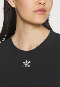 Musta ribakanga t-särk, millel on ümmargune kaelus ja lühikesed varrukad. Rinnal on valge broderi näidisega Adidas'i trefoil logo.