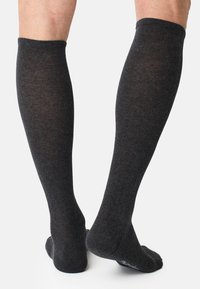 Grå knæhøje sokker med ribbet tekstur. Blødt strikkemateriale med en subtil glans. Designet inkluderer en glat manchet øverst.