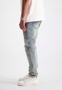 Lichtblauwe denim jeans met een slim fit, lichte vervaagde details, gecombineerd met witte sneakers. De stof heeft een zachte textuur.