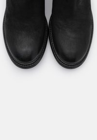 Botas de tobillo negras con un acabado de cuero suave, punteras redondeadas y una costura a lo largo de la suela. Diseño minimalista sin hardware visible.