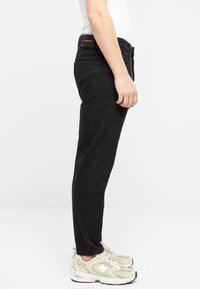 Jeans de mezclilla negra con un corte ajustado, piernas ligeramente entalladas, diseño de cinco bolsillos y costuras naranjas contrastantes en la cintura.