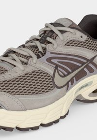 Γκρι και καφέ παπούτσι για τρέξιμο Nike με πλέγμα στο πάνω μέρος, επενδεδυμένη σόλα και δεμένα κορδόνια, εμφανίζεται υπό γωνία σε λευκό φόντο.