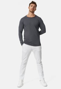 Camisa de manga larga gris con cuello redondo, combinada con pantalones blancos y zapatillas blancas, con un diseño ajustado y textura suave.