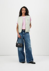 Gilet matelassé vert clair sur une chemise rose, associé à un jean bleu oversize. Les accessoires comprennent un sac à main noir avec un logo décoratif.