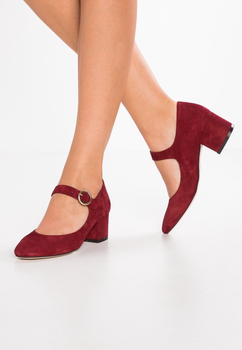 Talons Mary Jane en suède rouge avec un bout rond, présentant un design en découpe, un talon block épais et une sangle avec boucle circulaire.