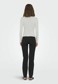 White ribbed long-sleeve top with a fitted design paired with black straight-leg jeans. Model is wearing flat sandals, viewed from the back.