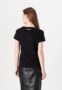 Juodas trumpas rankovėmis marškinėliai su apvaliu iškirpimu ir glotniu paviršiumi. Ant nugaros yra baltas "KARL LAGERFELD" logotipas.