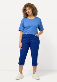 T-shirt cropped bleu avec des manches roulées, associé à un pantalon bleu fuselé. Les deux vêtements présentent une texture lisse et un design décontracté.
