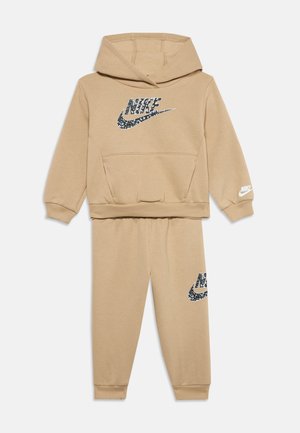 Ensemble beige Nike sweat à capuche et pantalon assorti pour enfants, avec des impressions de logos noirs et blancs sur la poitrine, le pantalon et la manche.