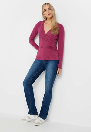 Top envolvente de manga larga en rosa oscuro, combinado con vaqueros azules y zapatillas blancas. Presenta un diseño ajustado y una textura de tela suave.