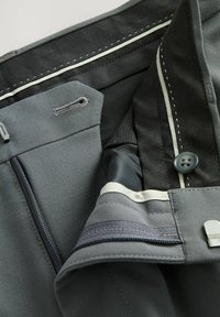 Tejido gris con cremalleras, botones y detalles de costura. Parcialmente forrado con acentos en contraste y una textura interior suave.