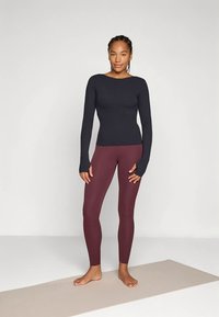 Black fitted long-sleeve top with thumbholes paired with maroon leggings. Both are made of stretch fabric and have a smooth texture.