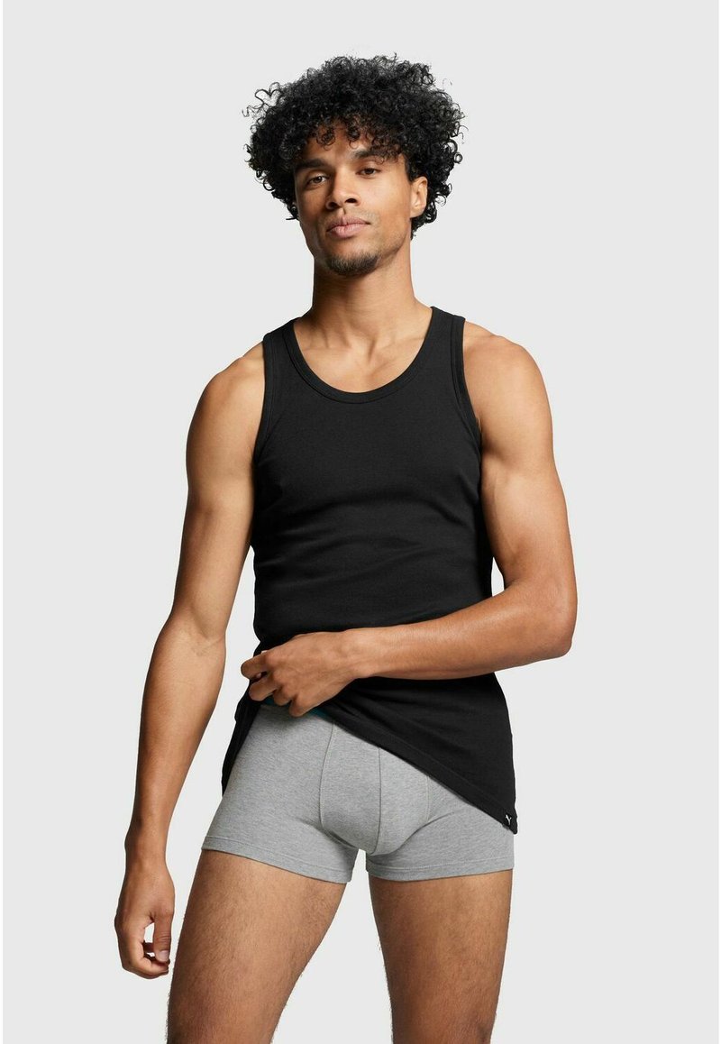 Black cotton tank top with a round neckline, worn over gray boxer briefs. The model has curly hair and is positioned facing forward.