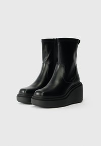 Bottines en cuir noir avec une semelle compensée, dotées d'une fermeture éclair sur le côté, d'une texture lisse et d'un design à bout arrondi.