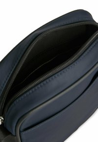 Borsa blu navy con esterno liscio e zip nera. Si apre su un interno foderato con un unico scomparto per lo stoccaggio.