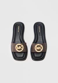Sorte slides-sandaler med en rektangulær form, der har en brun strop af stof pyntet med en gylden cirkulær MK-logo. Tekstureret indersål.