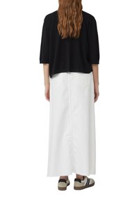 Zwart cropped top, witte lange rok en sneakers. De top heeft een losse pasvorm, terwijl de rok een rechte stijl heeft met achterzakken.