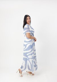 Robe maxi avec un motif abstrait bleu et blanc fluide, courtes manches évasées, taille smockée et tissu léger et transparent.