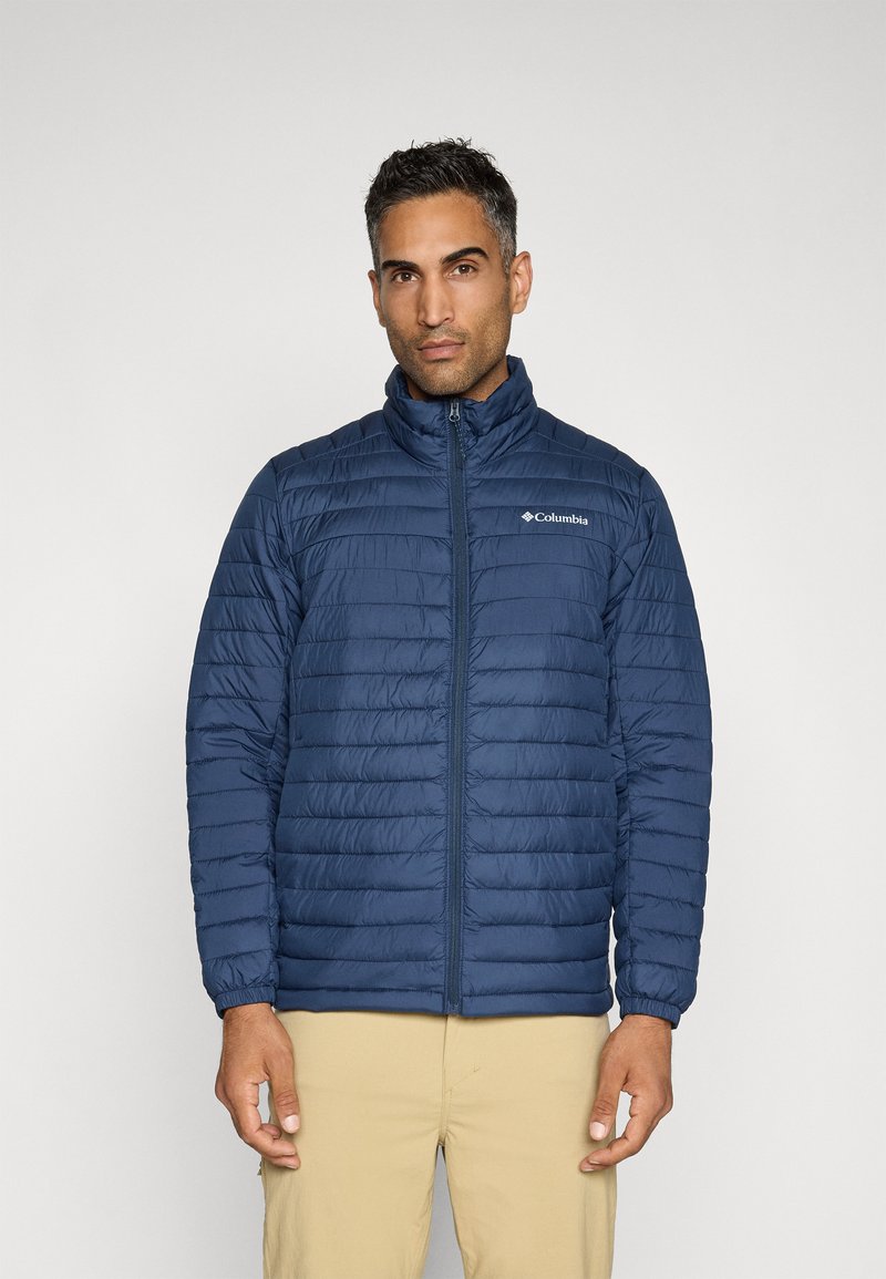 Veste matelassée zippée bleu marine avec un motif matelassé horizontal, col haut et poignets élastiques. Présente le logo Columbia sur la poitrine gauche.