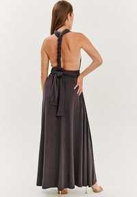 Maxi šaty z tmavo šedej látky, s halter krkom, opleteným detailom na chrbte a zauzleným pásom. Hladká textúra, voľný silueta, až po členky.