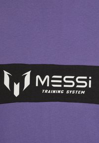 Lilla treningsskjorte med en svart stripe og hvit tekst "MESSi TRAINING SYSTEM" samt en logo, laget av mykt stoff med en glatt tekstur.
