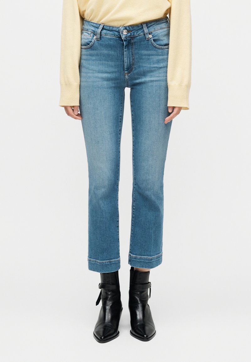 Γυναίκα που φοράει ανοιχτό μπλε cropped τζιν με ίσια μπατζάκια, μπεζ τοπ μακρυμάνικο και μαύρα μποτάκια αστραγάλου με μυτερή μύτη και αγκράφες.