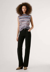 Večbarvni pleteni breztežni pulover z visokim ovratnikom, kombiniran s črnimi razširjenimi hlačami in svetlo rjavimi gležnarji s peto.