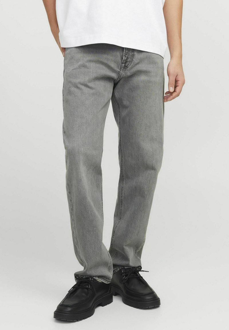Graue Denim-Jeans mit geradem Schnitt, leichter Ausbleichung und Kontrastnähten. Kombiniert mit schwarzen Schnürschuhen und einem weißen Oversized-T-Shirt.