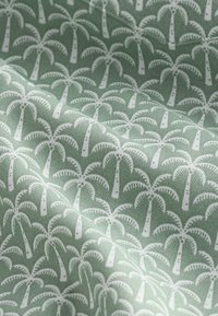 Grüner Stoff mit einem sich wiederholenden weißen Palmenmuster, zeigt Textur und sanfte Falten.